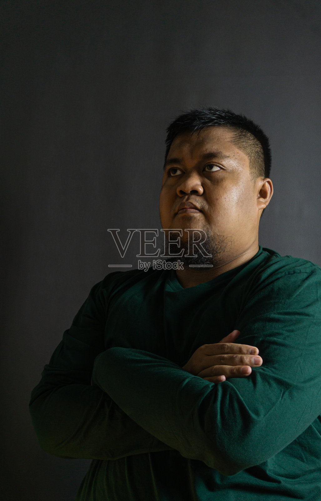 身穿森林绿长袖衬衫的男子,双臂交叉于胸前站立,背景为黑色,自信的姿态代表着权威和态度。照片摄影图片