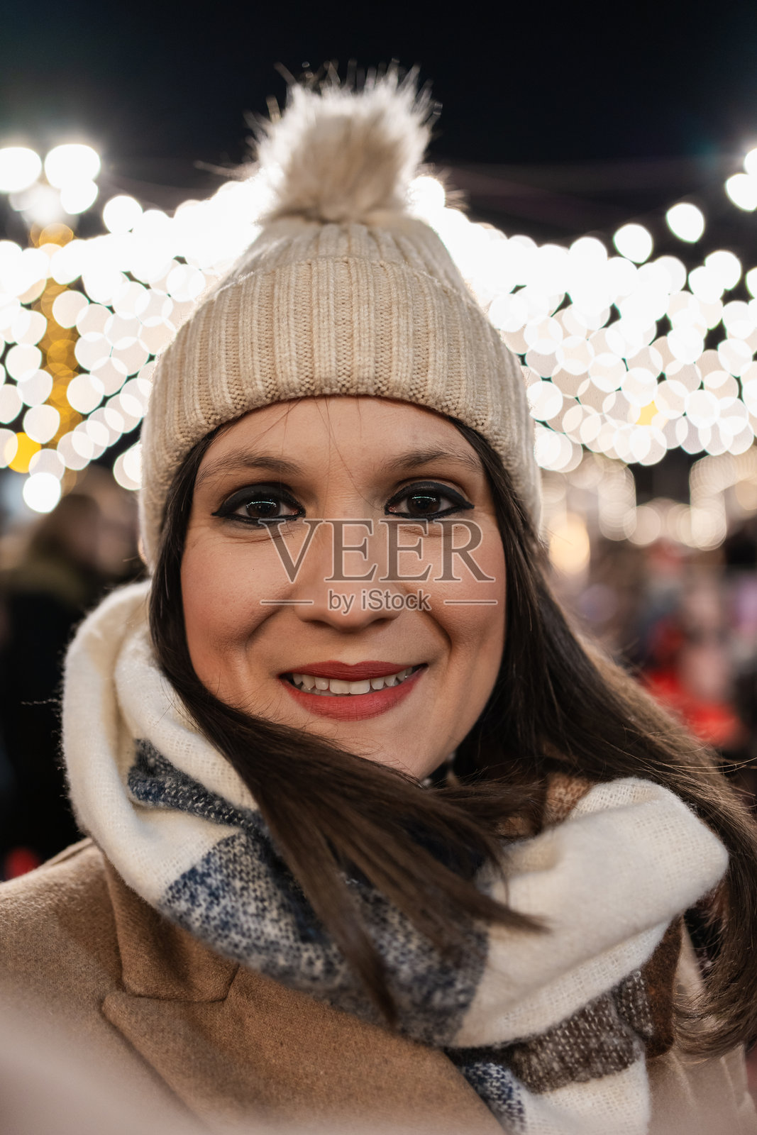 女人在圣诞集市上微笑,背景是模糊的灯光。照片摄影图片