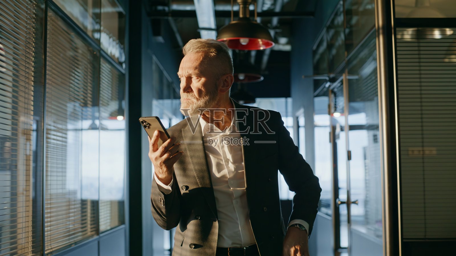 一位面露担忧的专业人士站在办公室走廊里,手里拿着手机。他看起来很紧张,是一名资深人士。照片摄影图片