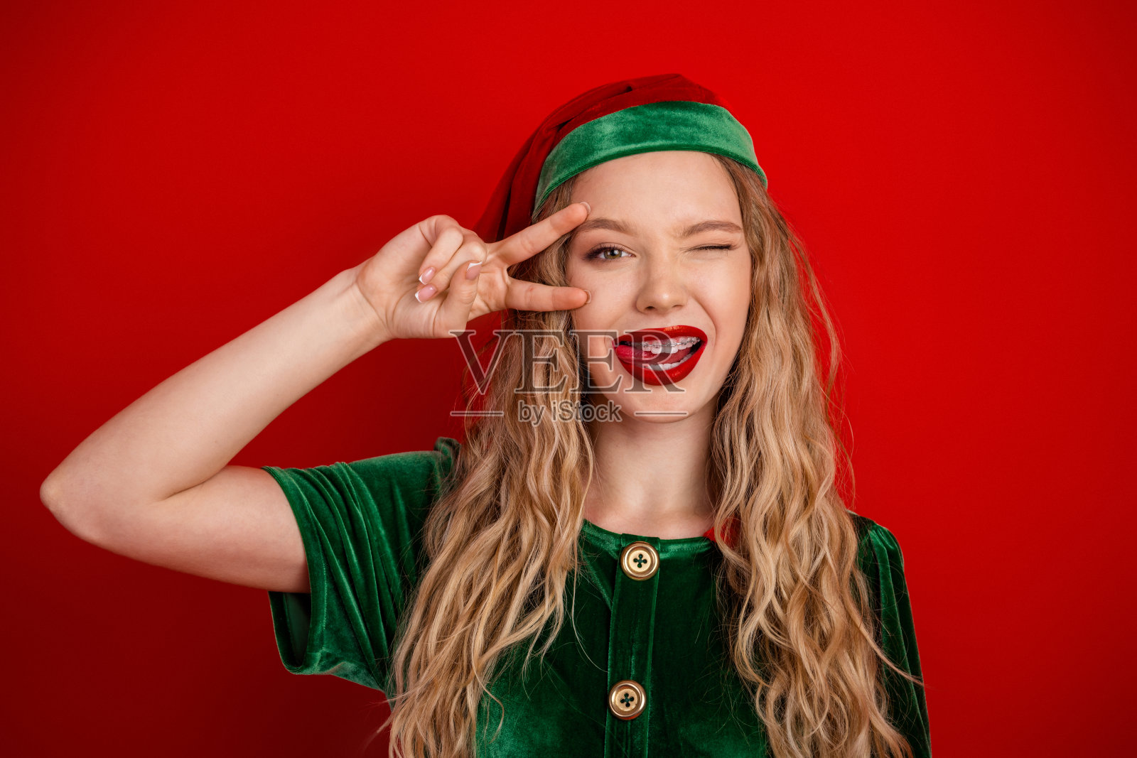 节日里,身着精灵服装的年轻女子在充满活力的红色背景前自信地摆姿势,背景是节日季。照片摄影图片