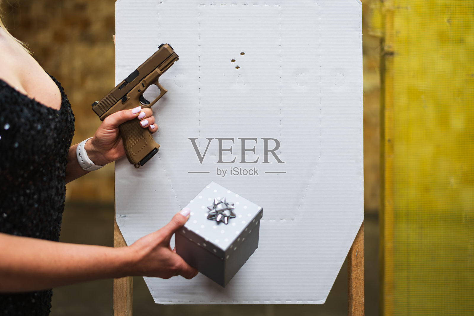 一位身着节日服装的女士在射击场手持手枪和礼品盒,一个独特的礼物概念。照片摄影图片