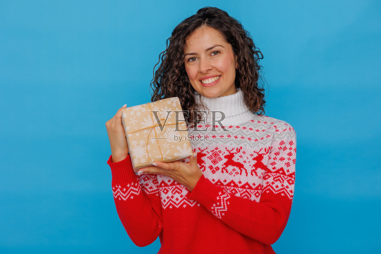 穿着圣诞毛衣的快乐年轻女子收到节日礼物,站在蓝色背景前照片摄影图片
