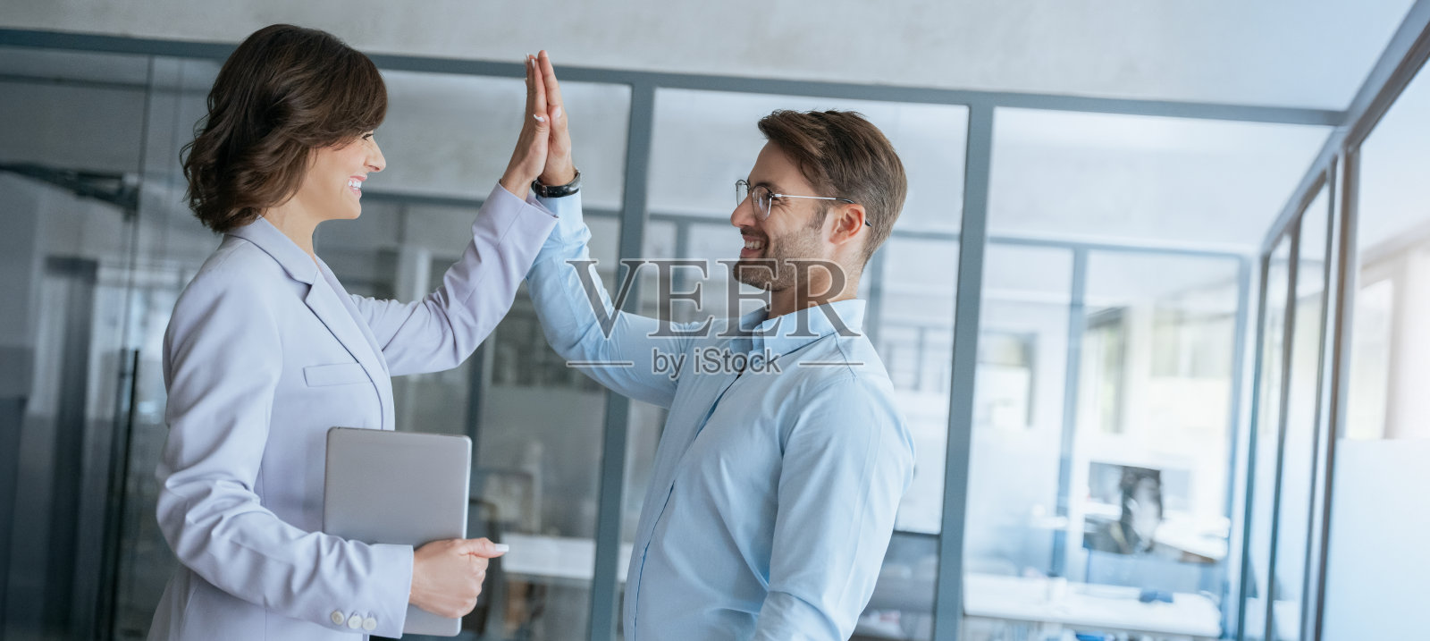 笑容满面的成功欧洲团队,包括一名男士和一位成熟专业的女士,正在庆祝取得优异成绩。商界人士在办公室工作空间中击掌庆贺。留有复制空间。照片摄影图片