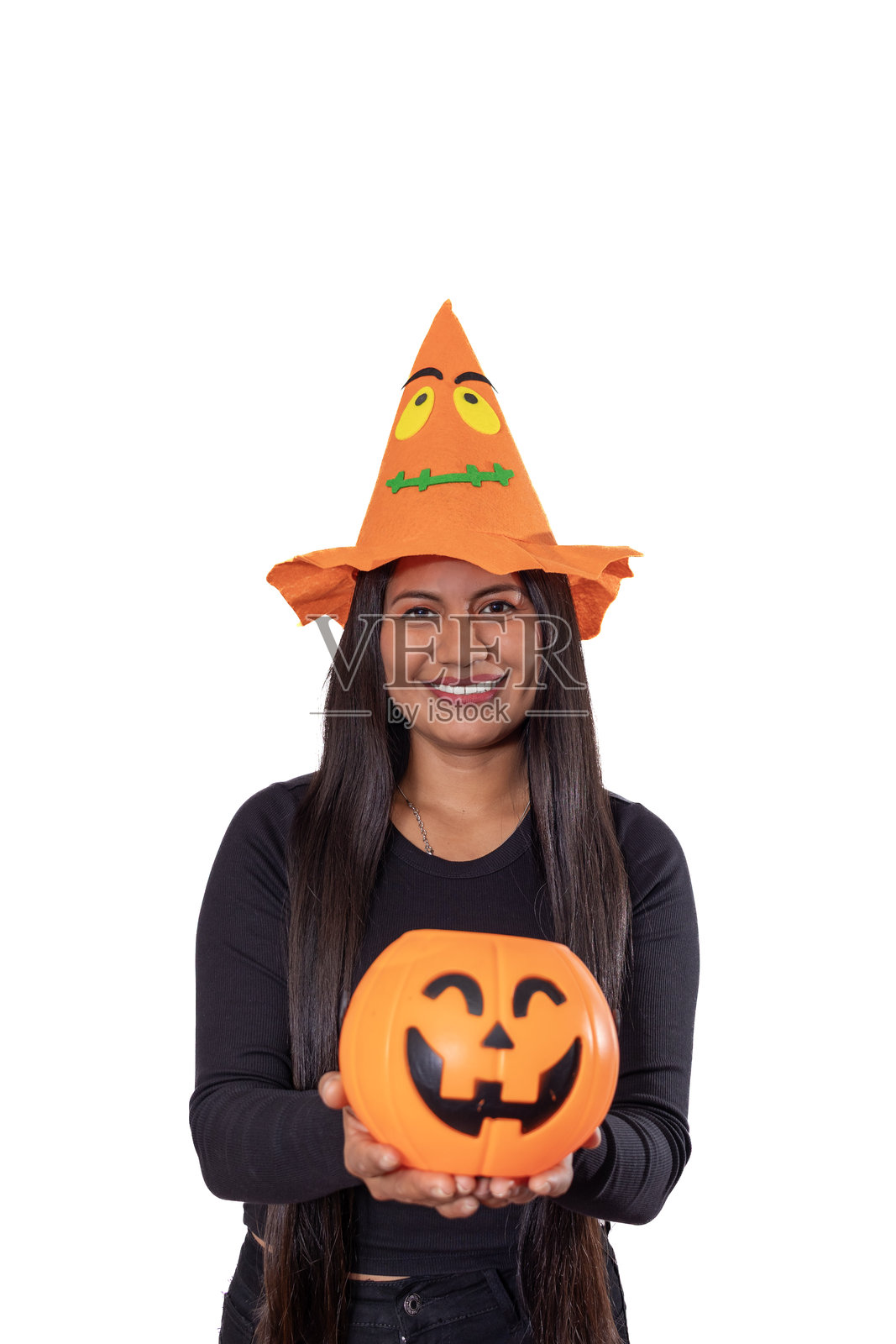 一位戴着节日南瓜帽、手持橙色杰克灯笼糖果桶的女性,在白色背景前充满活力地庆祝万圣节。照片摄影图片