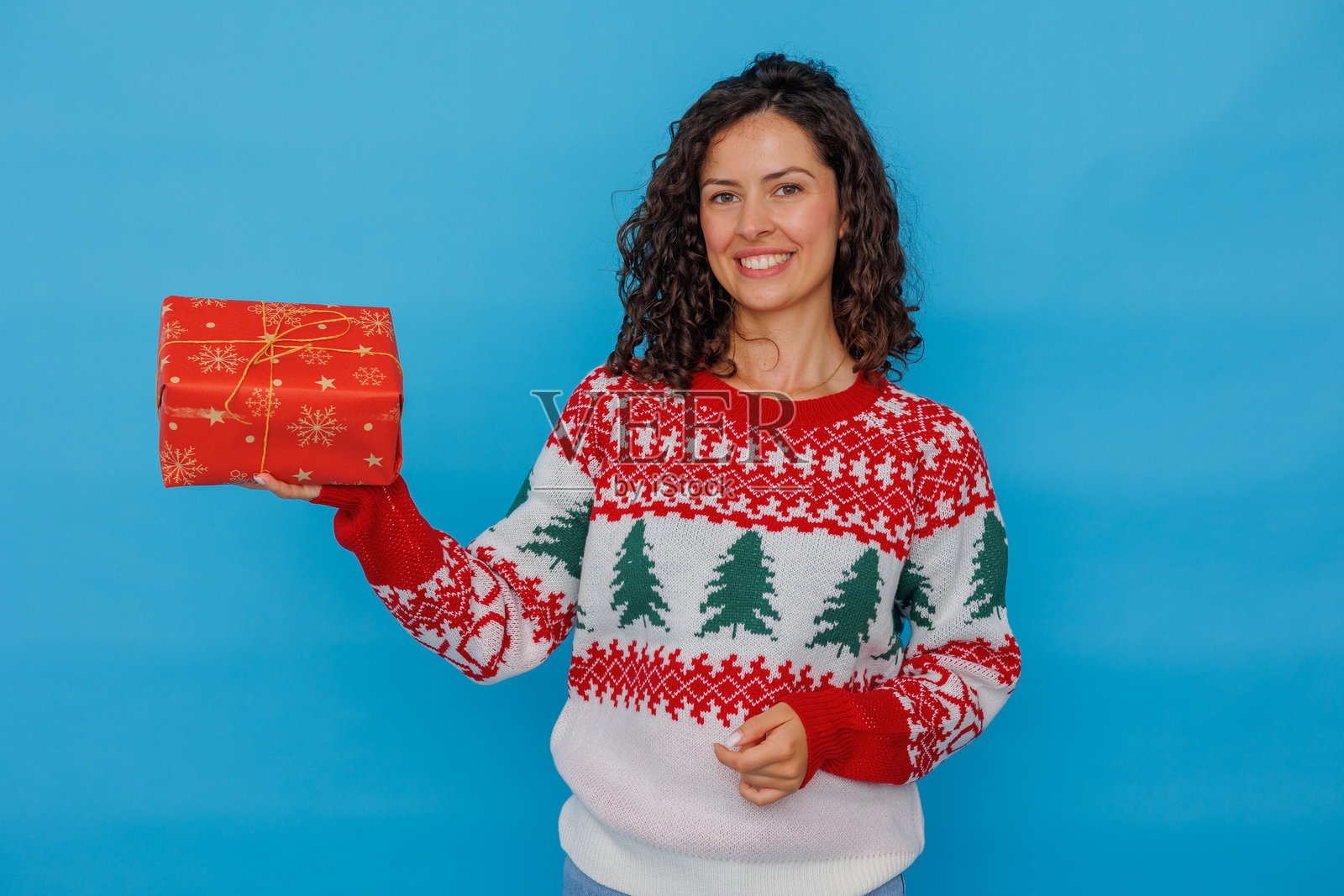 一位女士在节日季微笑着,穿着节日毛衣,手里拿着圣诞礼物。照片摄影图片