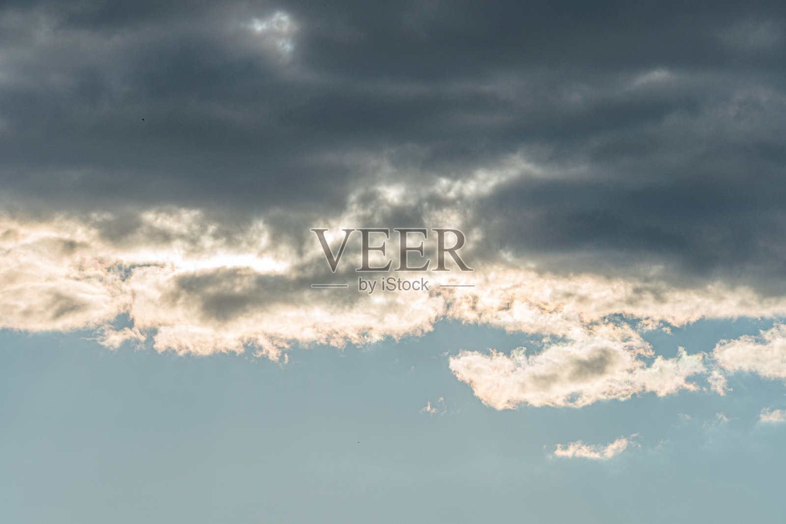 戏剧性的暴风雨天空,带有深灰色、纹理感的云层,有几处浅蓝色缝隙,暗示着阳光。冷色调占主导,浅蓝色缝隙带来了微妙的对比。写实风格捕捉了深度感。照片摄影图片