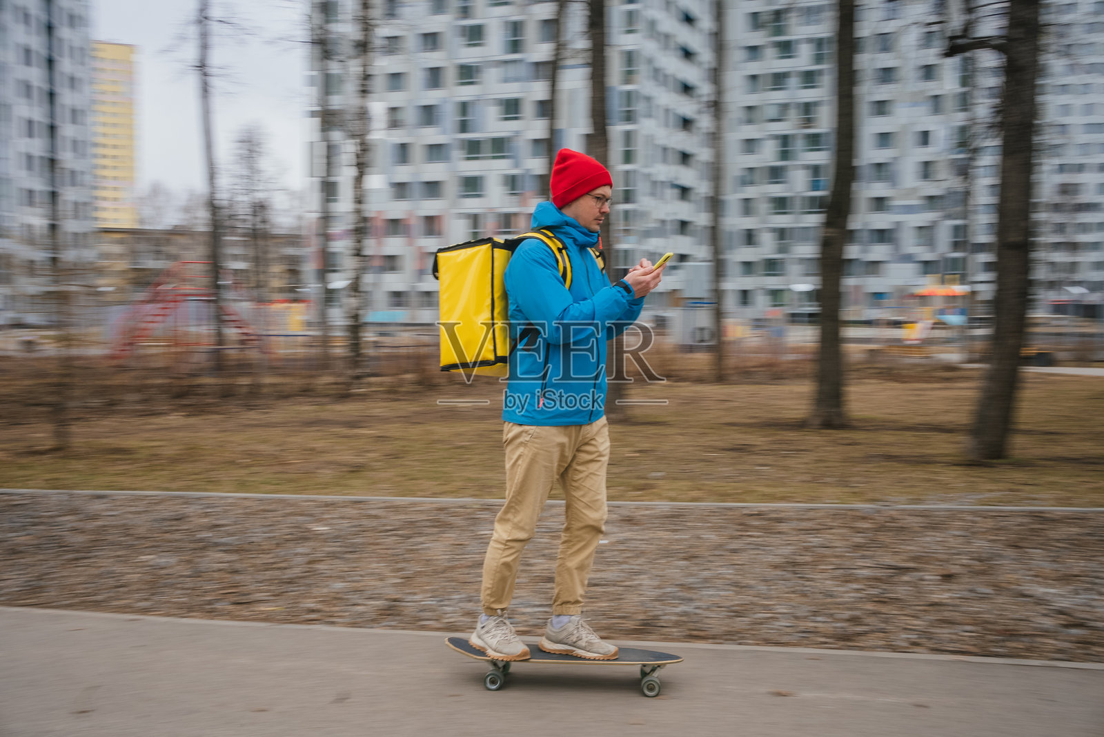 骑滑板车的快递员穿梭于城市公园,身背黄色保温背包,通过智能手机应用程序查看数字订单照片摄影图片