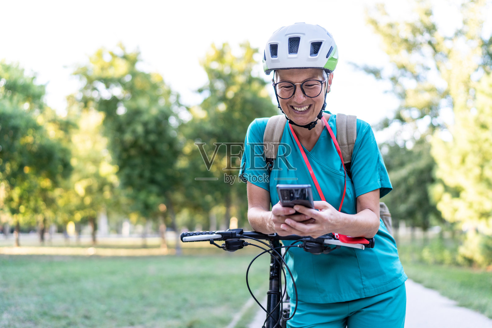 一位成熟的女医护人员在公园骑自行车并使用智能手机照片摄影图片