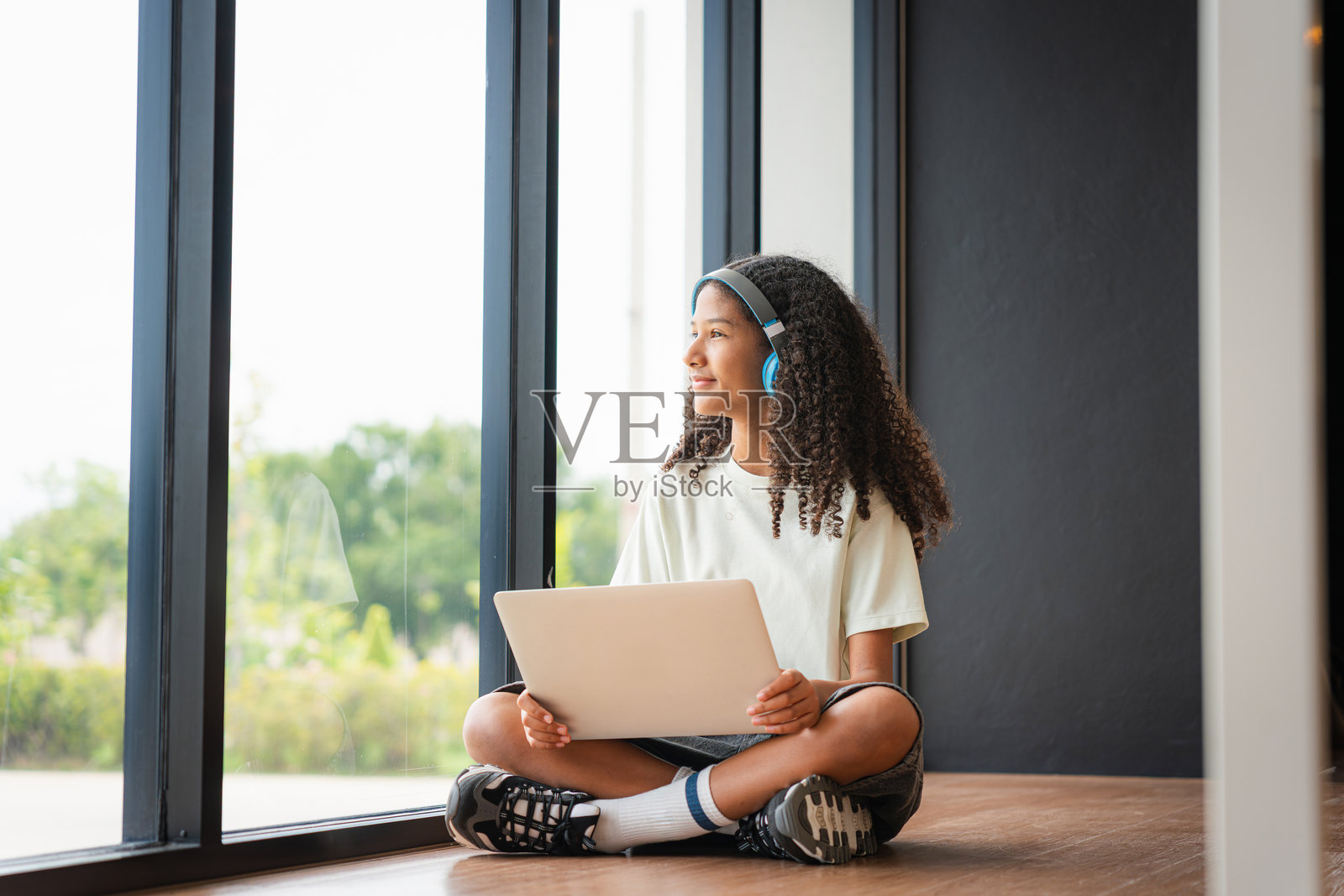 年轻学生享受音乐和学习时光,快乐女孩在窗边用科技放松,戴着耳机和笔记本电脑的少女望着窗外照片摄影图片