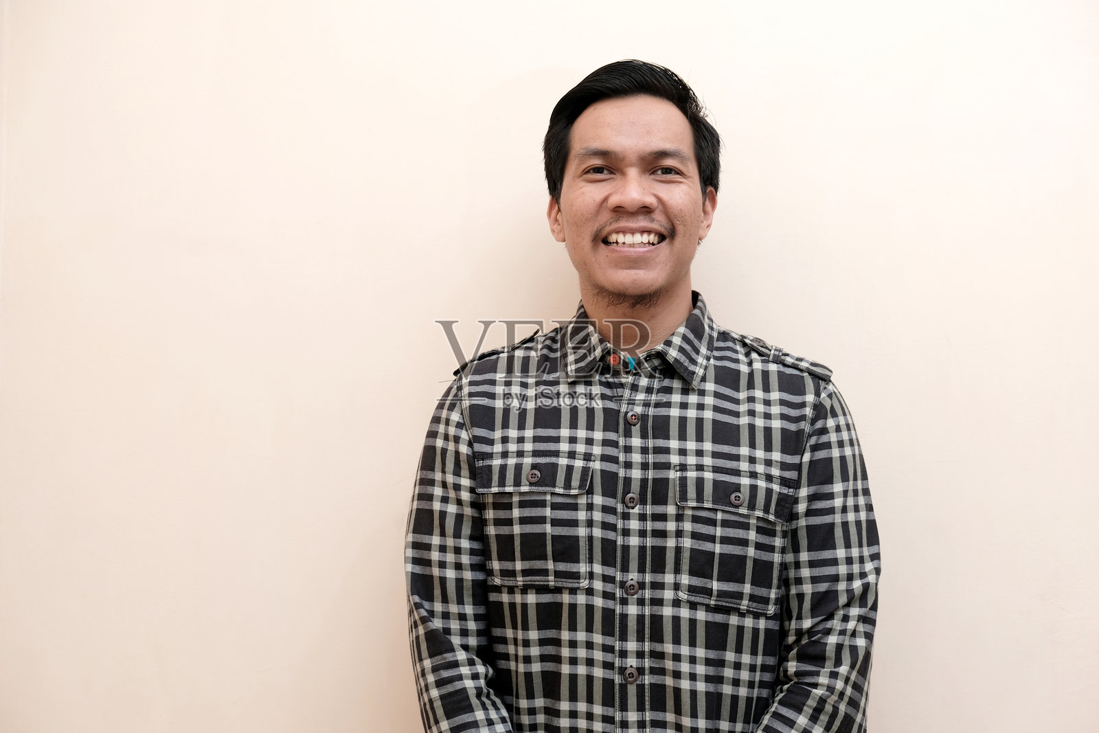 一位东南亚男子穿着法兰绒衬衫站着,面带微笑,表情快乐。照片摄影图片