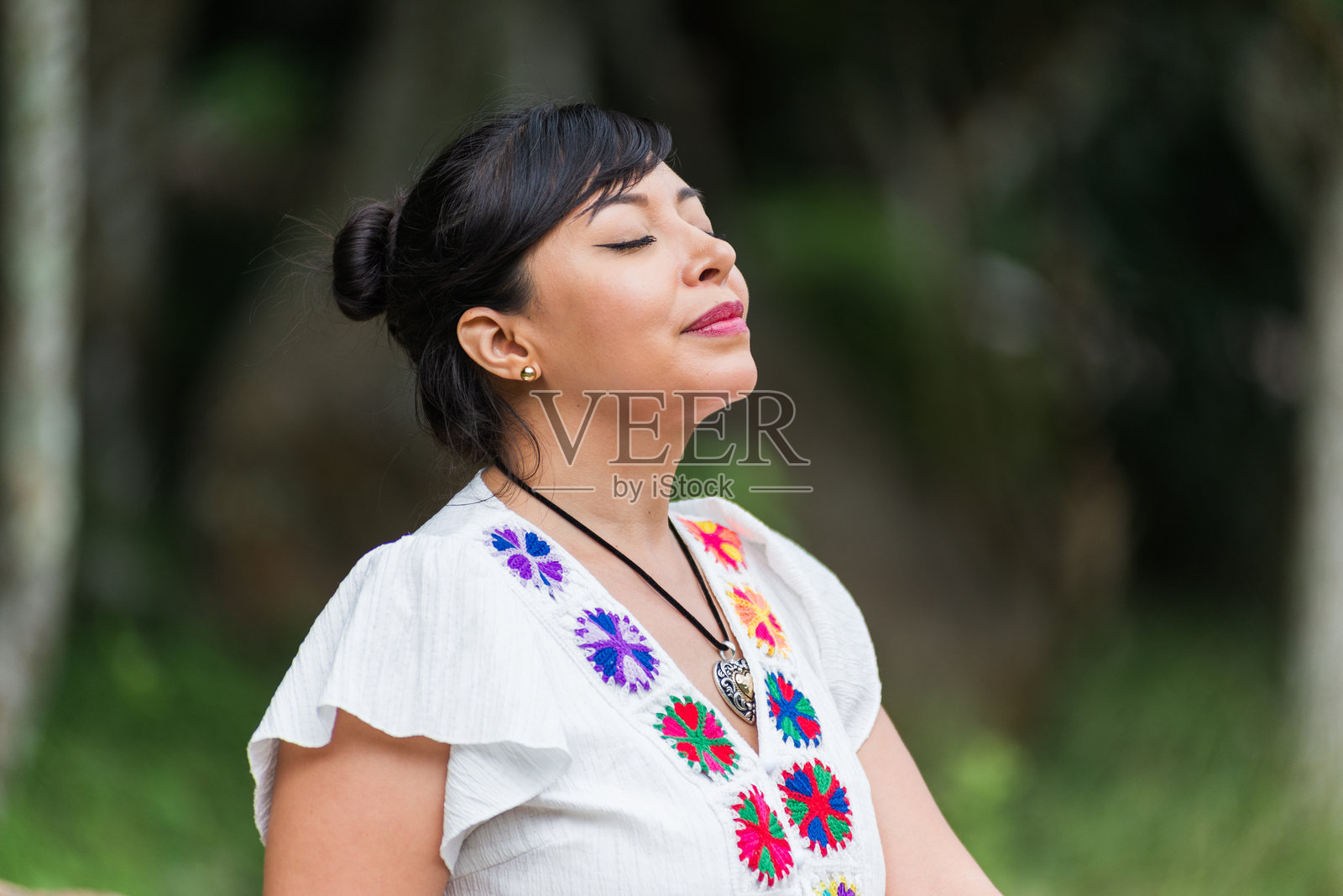 一位身穿白色刺绣衬衫的女士在户外闭着双眼。照片摄影图片