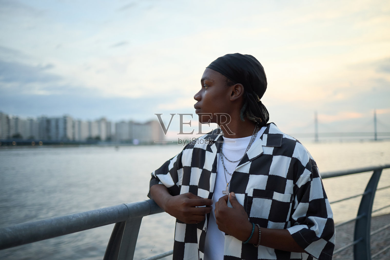 年轻的黑人成年男子站在水边,沉思着城市天际线照片摄影图片