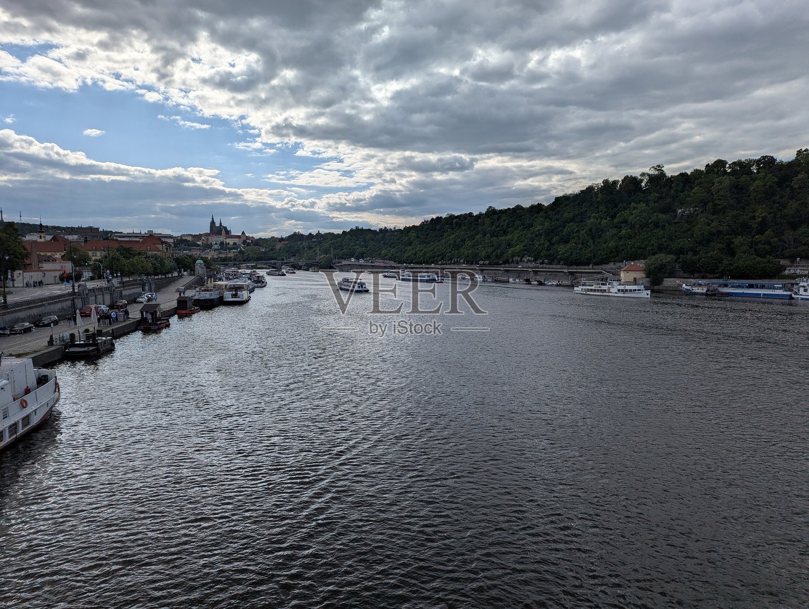 远处的船只和历史悠久的布拉格天际线旁的伏尔塔瓦河照片摄影图片