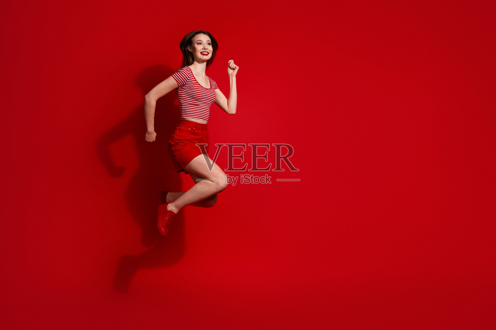 穿着时尚休闲红装的活力年轻女子在鲜艳的红色背景前快乐地跳跃,展现出热情照片摄影图片