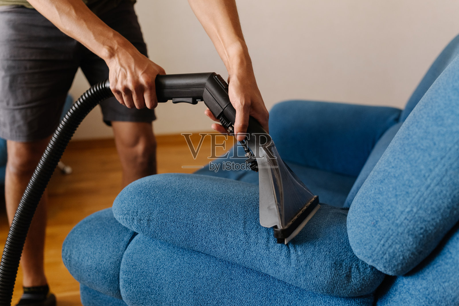 现代客厅里,一名无法辨认身份的清洁服务人员正在使用洗地吸尘器清洁蓝色沙发,特写镜头,仅展示局部。照片摄影图片