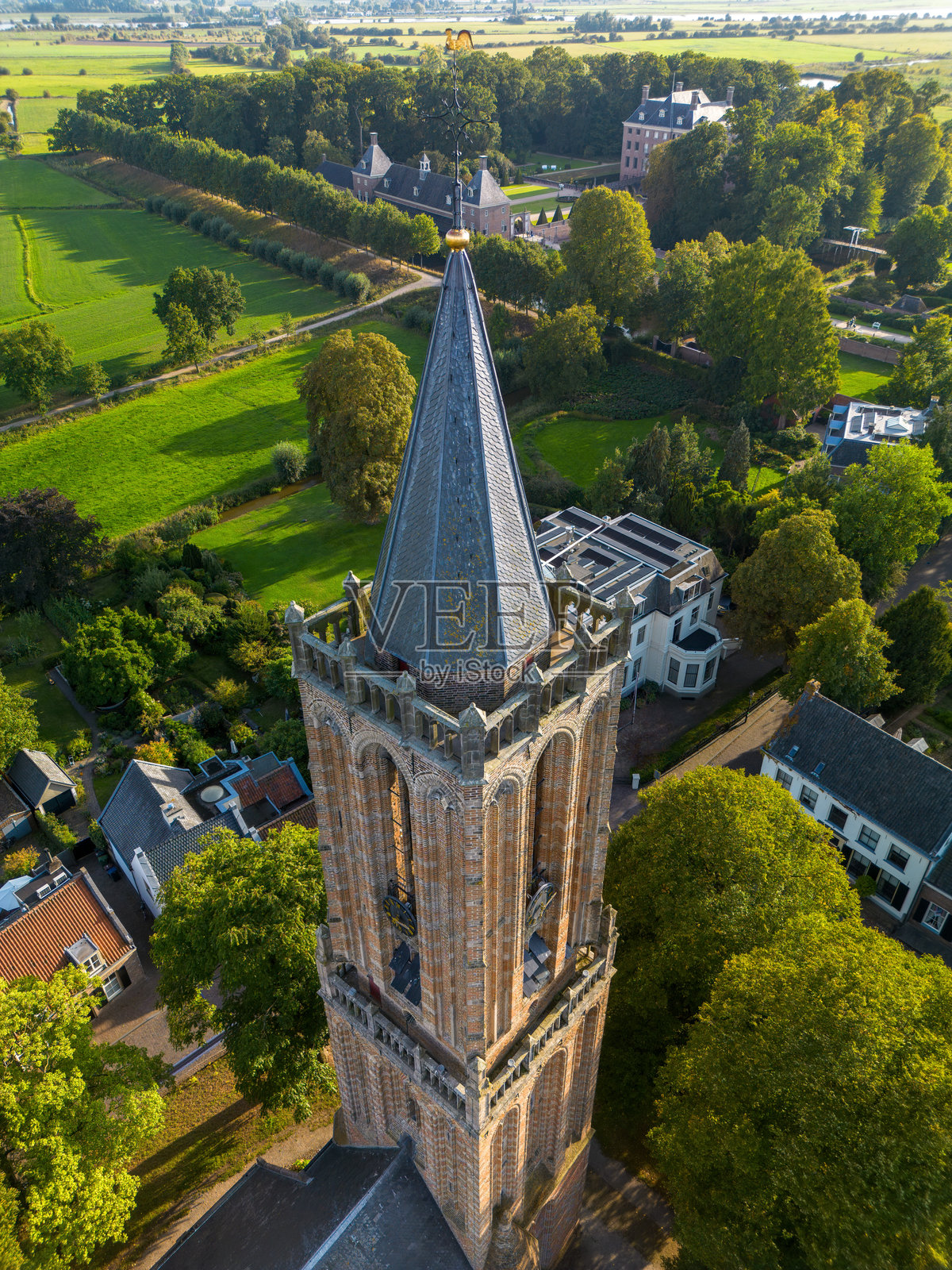 空中俯瞰哥特式砖砌教堂塔楼,拥有尖顶和尖塔,周围环绕着树木和住宅房屋,位于一个宁静的社区。照片摄影图片