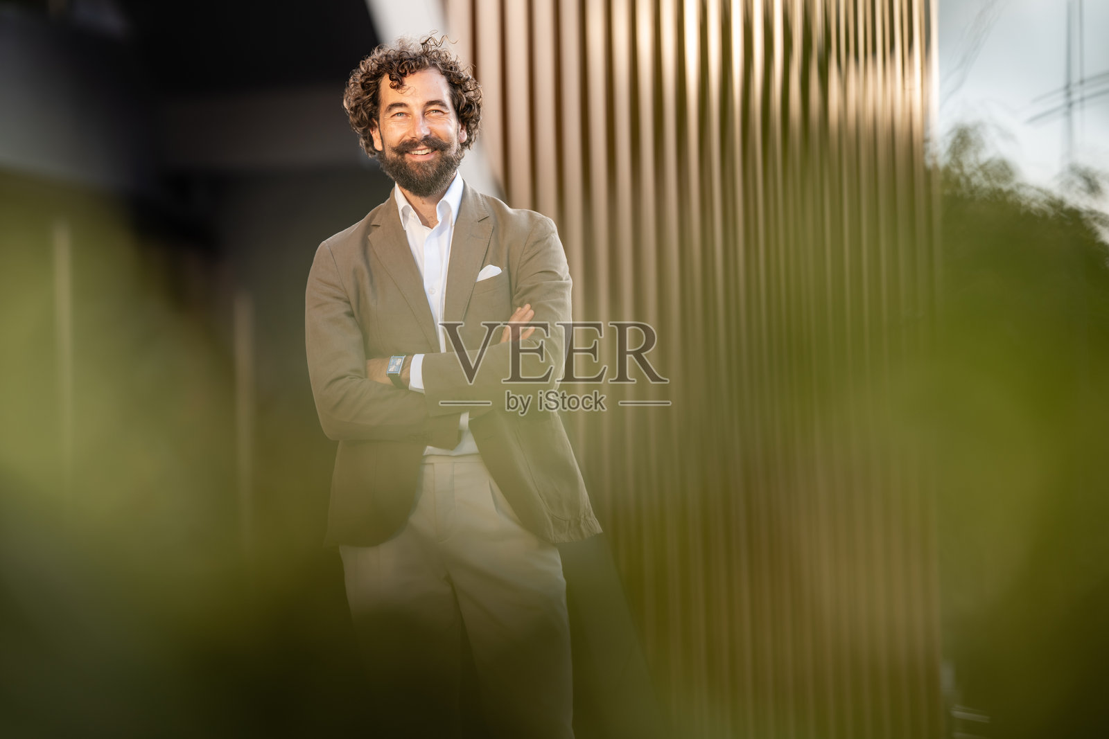 一位面带微笑、双臂交叉的商人正在现代建筑前摆姿势。照片摄影图片