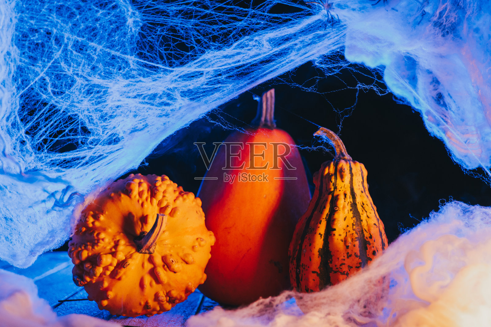 橙色的南瓜,笼罩在网络和烟雾中,在黑暗中发出幽蓝的诡异光芒,充满万圣节的氛围。照片摄影图片