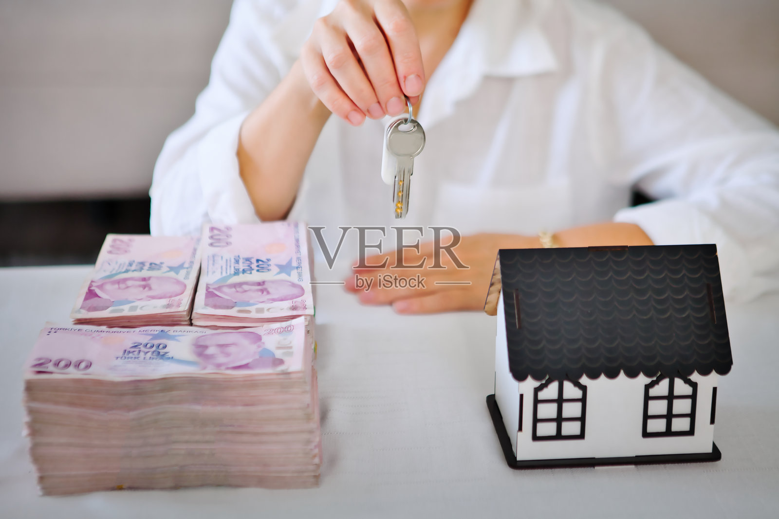 女房地产经纪人展示新房钥匙、一叠钱和房屋模型。照片摄影图片