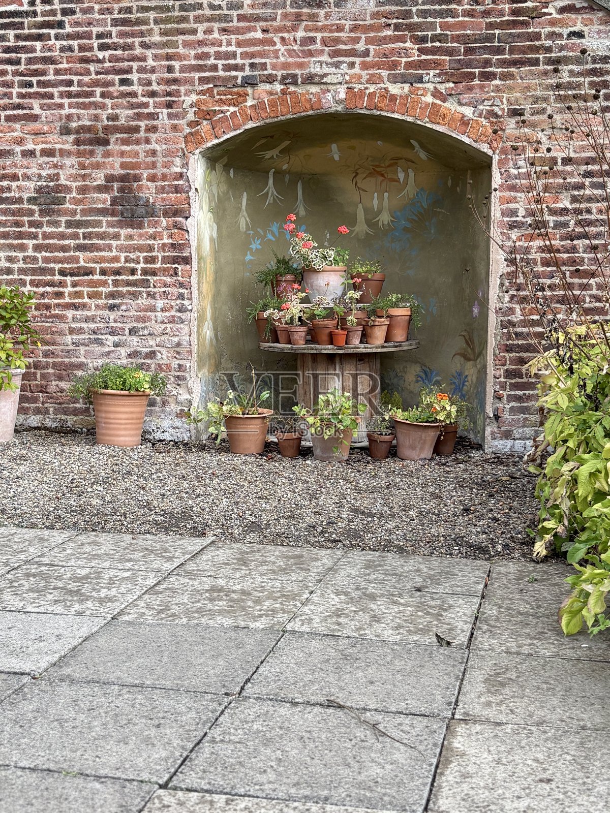 质朴的庭院展示:陶土花盆摆放在木卷轴桌上,置于拱形砖砌壁龛内。饱经风霜的墙壁作为背景,增添了这个复古庭院角落的魅力。照片摄影图片