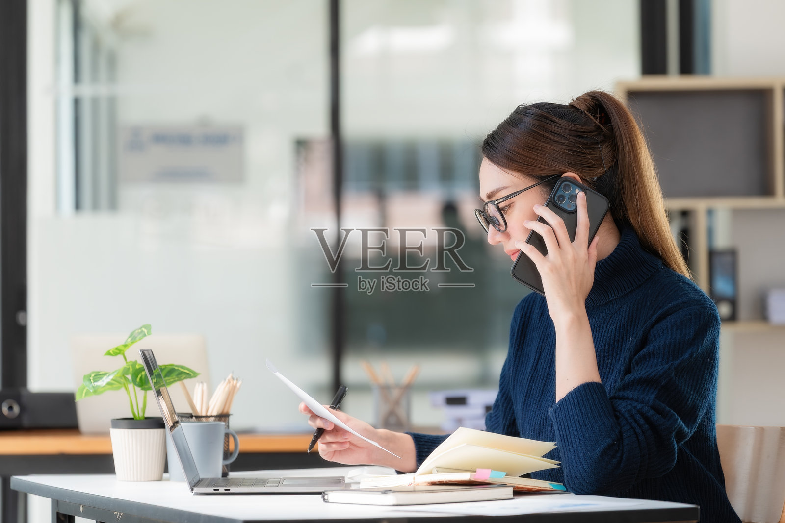一位亚洲女商人正在办公室里与她的商业伙伴通电话,处理或协商一笔生意。照片摄影图片