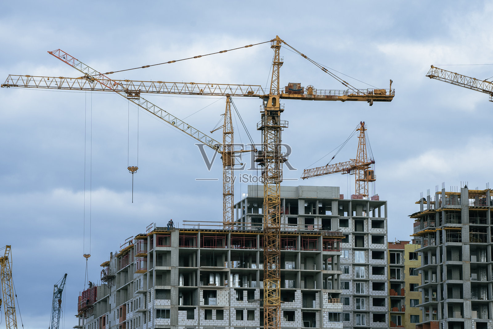 多个塔吊在一个大型建筑工地上作业,建造新的高层住宅楼,在多云的天空下象征着城市发展与增长。照片摄影图片