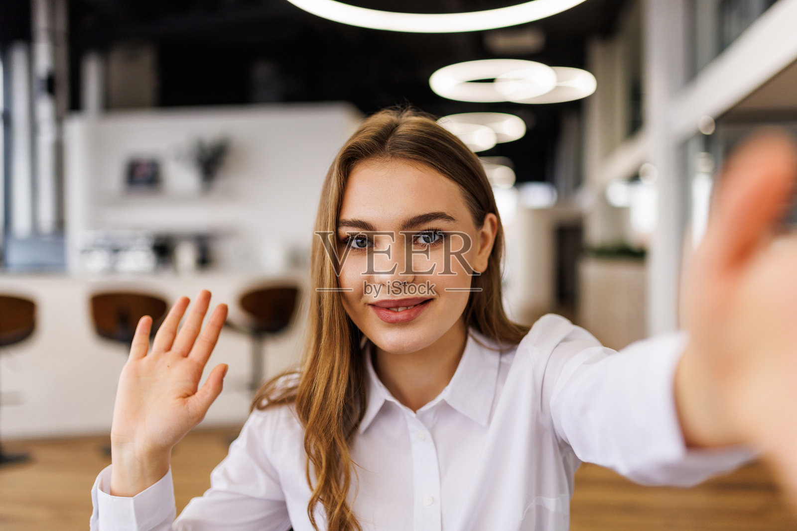 现代办公室里,一位女士在视频通话中微笑着挥手。照片摄影图片