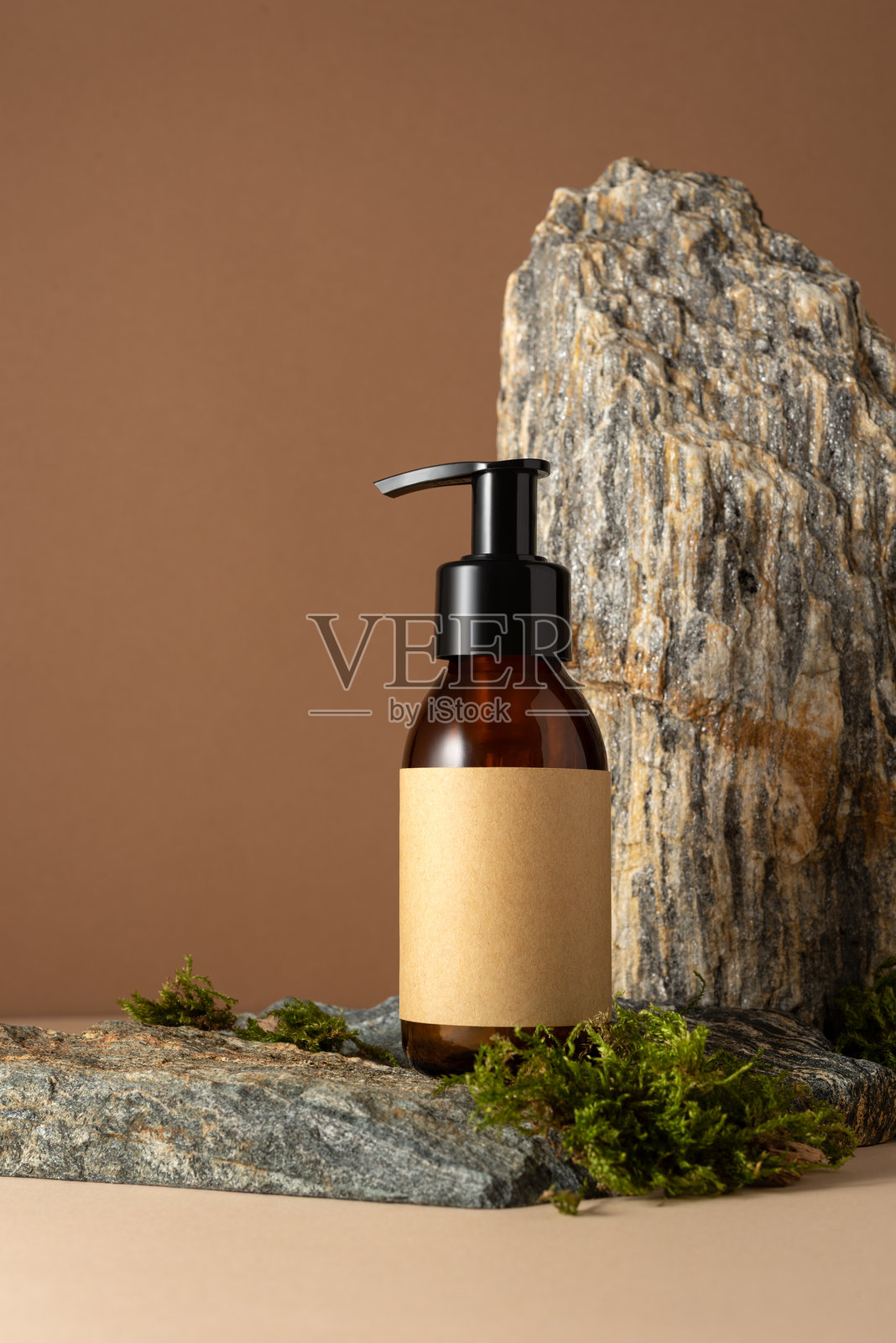 岩石讲台上的极简琥珀色化妆品泵瓶模型,带有空白牛皮纸标签照片摄影图片