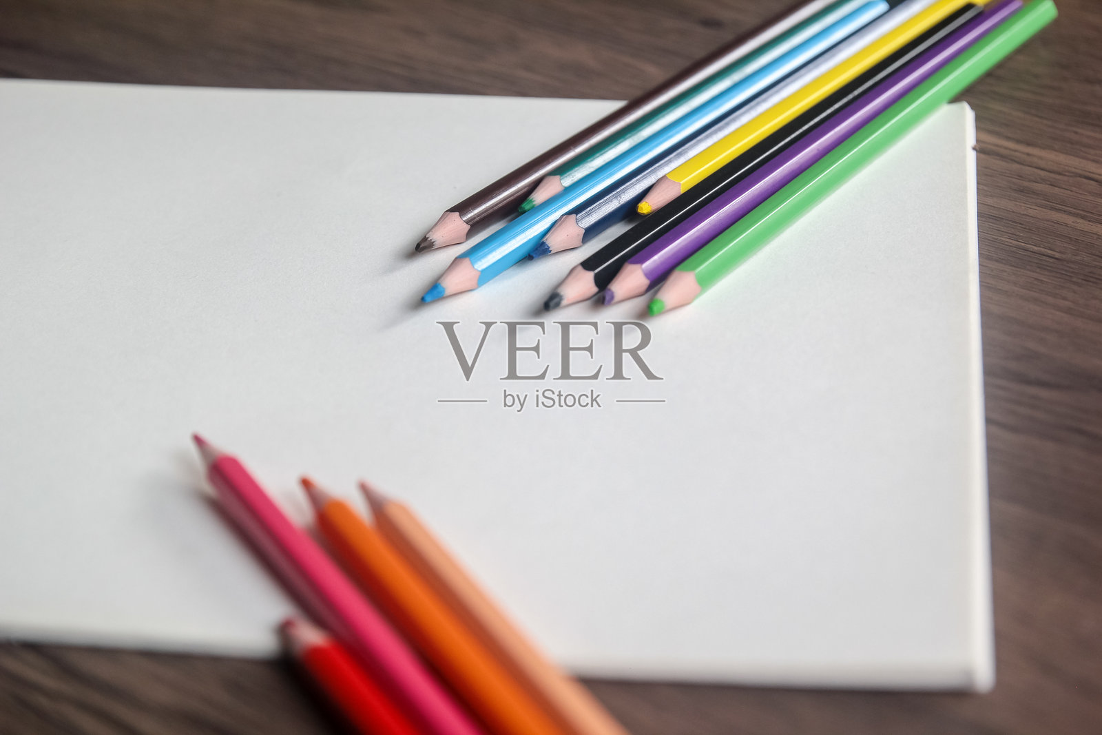 彩色的铅笔放在空白的白纸上,背景为木质照片摄影图片