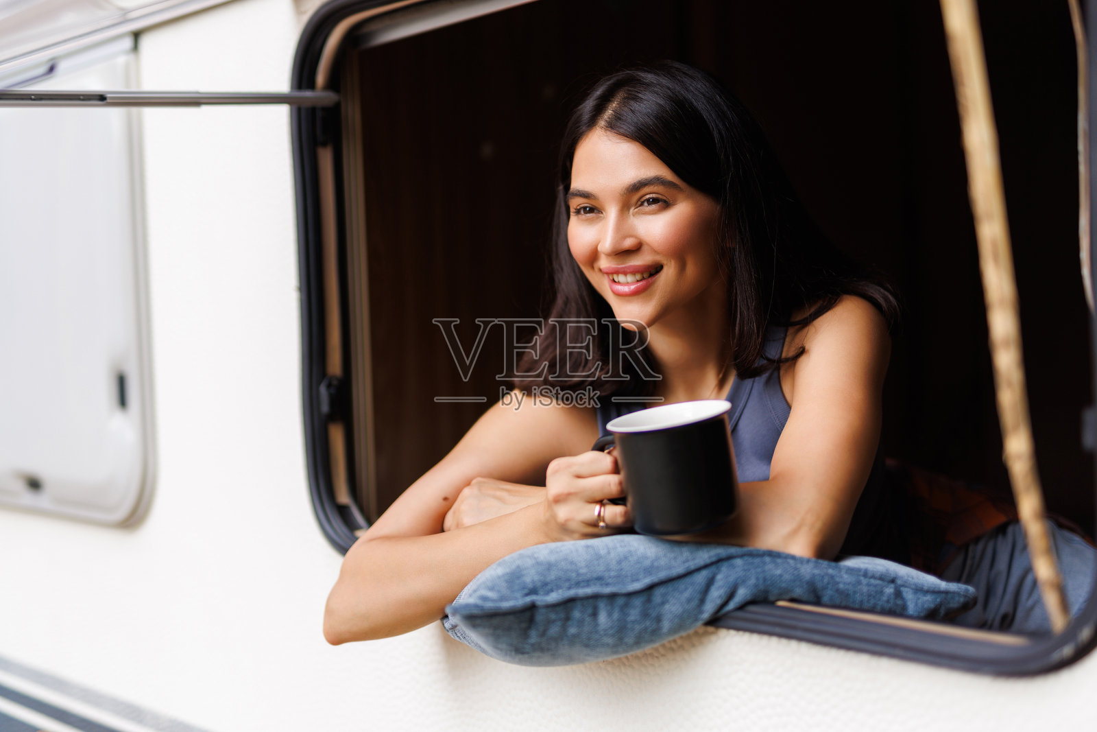 夏日里,一位美丽的年轻女子在露营车里手捧咖啡杯照片摄影图片