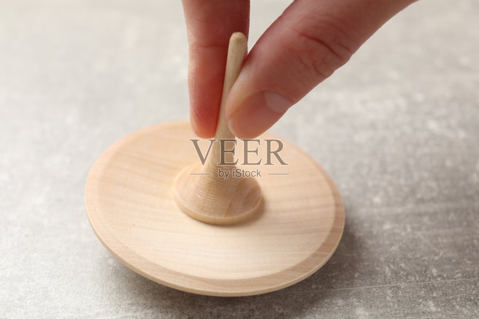 特写:一名女子在灰色纹理背景上玩木制陀螺。照片摄影图片