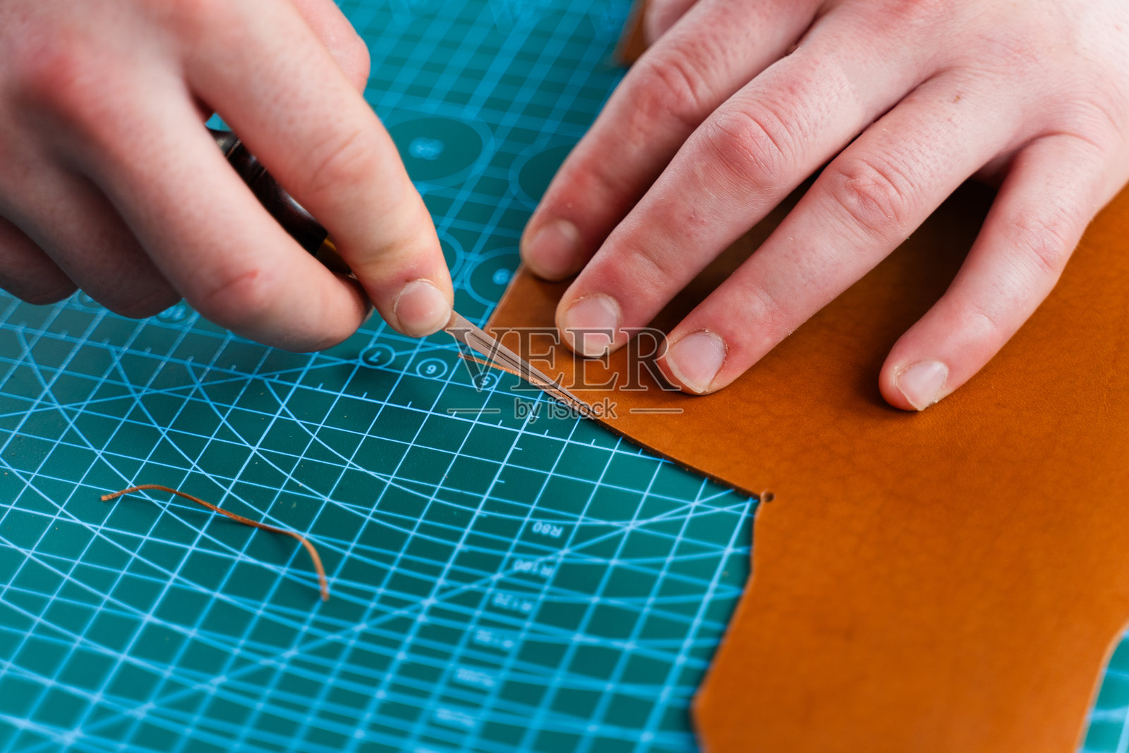 工匠用工具修剪皮革边缘,精确地修整切口。工匠用修边工具修整皮革边缘,确保曲线流畅,线条干净。照片摄影图片