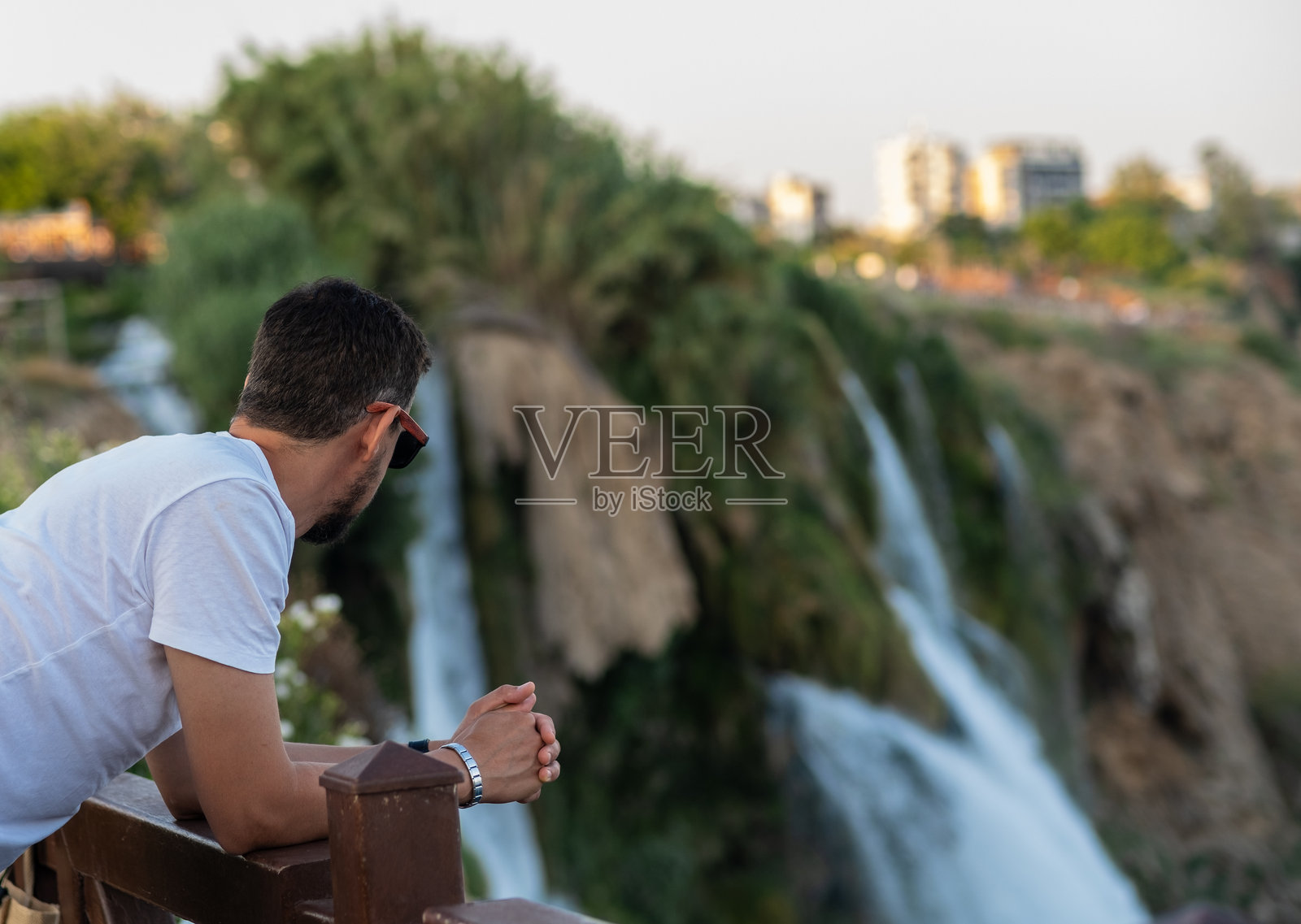 日落时分,男子在郁郁葱葱的自然环境中,从观景点欣赏美丽的瀑布。照片摄影图片