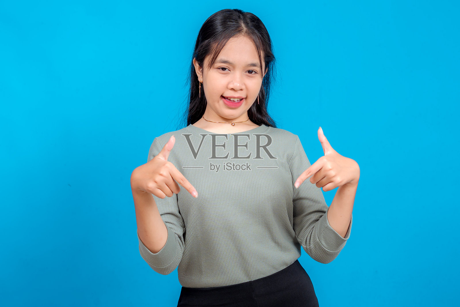 一位年轻的亚洲女性自信地笑着,双手食指指向下方。她富有表现力的面部表情和手势暗示着行动号召或宣传信息放置。照片摄影图片