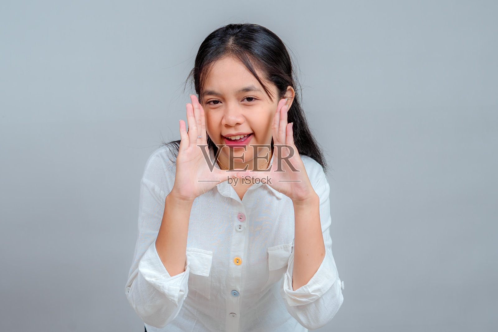 一位快乐的年轻亚洲女性在影棚肖像照中,双手做出大声呼喊的姿势,俏皮地笑着,表达着热情、兴奋和沟通。照片摄影图片