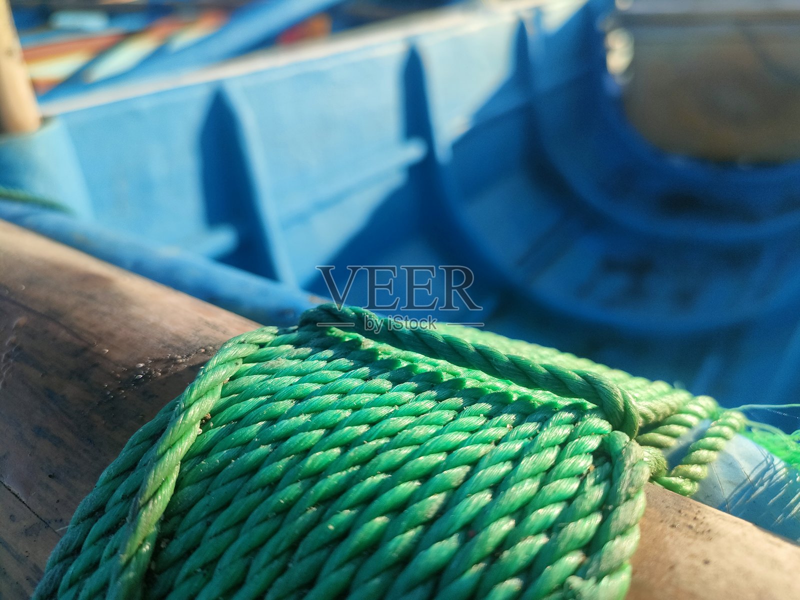 close-up of green rope coiled around a wooden beam on a blue boat照片摄影图片