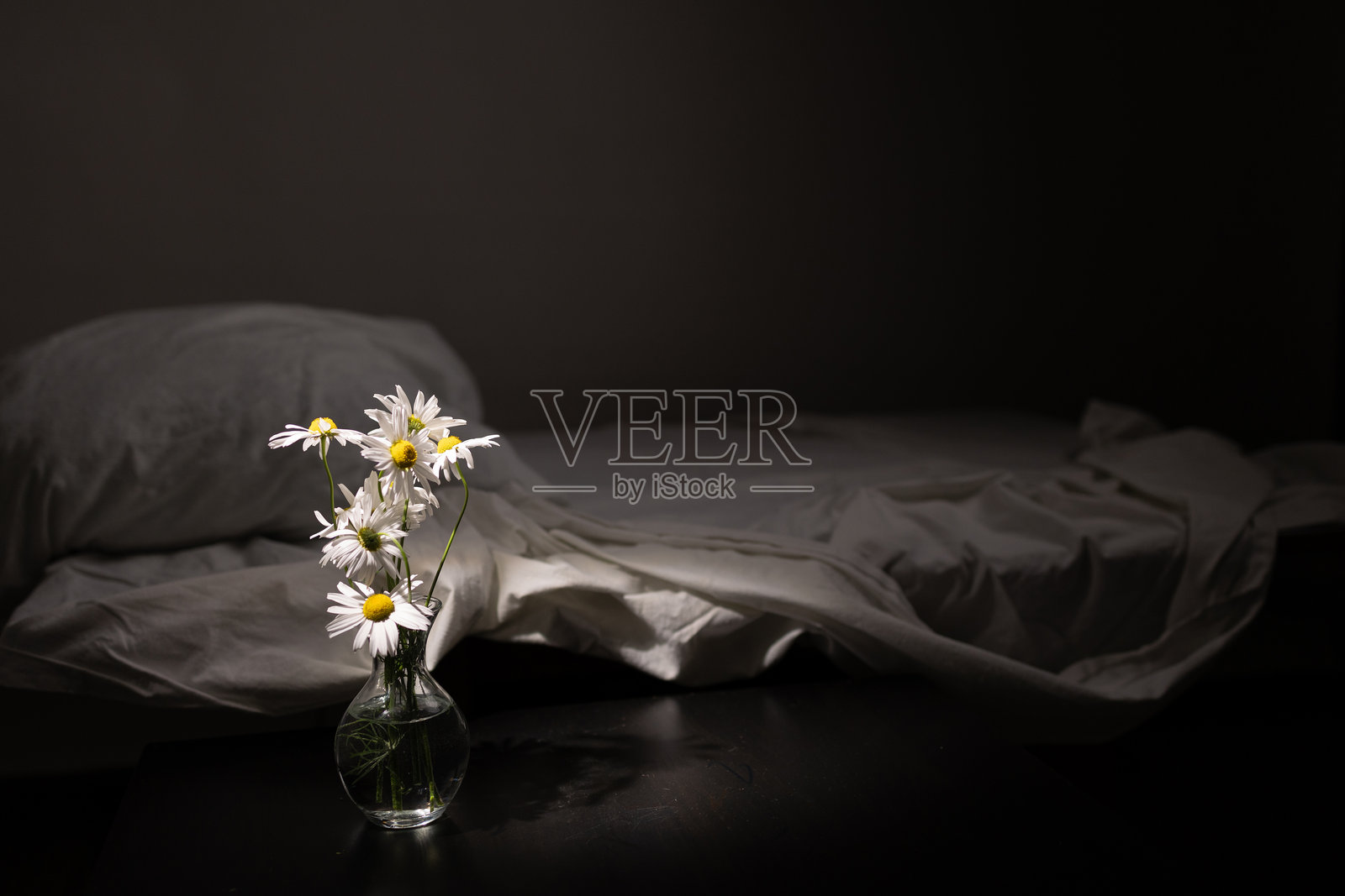 黑色表面上的玻璃花瓶雏菊靠近白色床单照片摄影图片