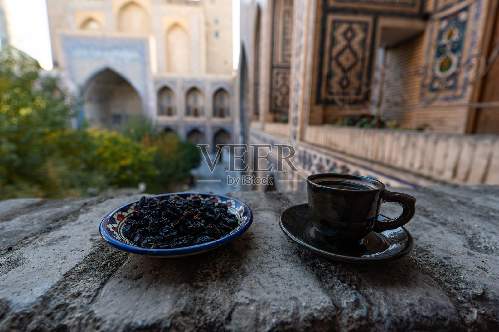 桌子上放着一个黑色的马克杯,背景是美丽的中古建筑。杯子里是乌兹别克风格的黑咖啡。照片摄影图片