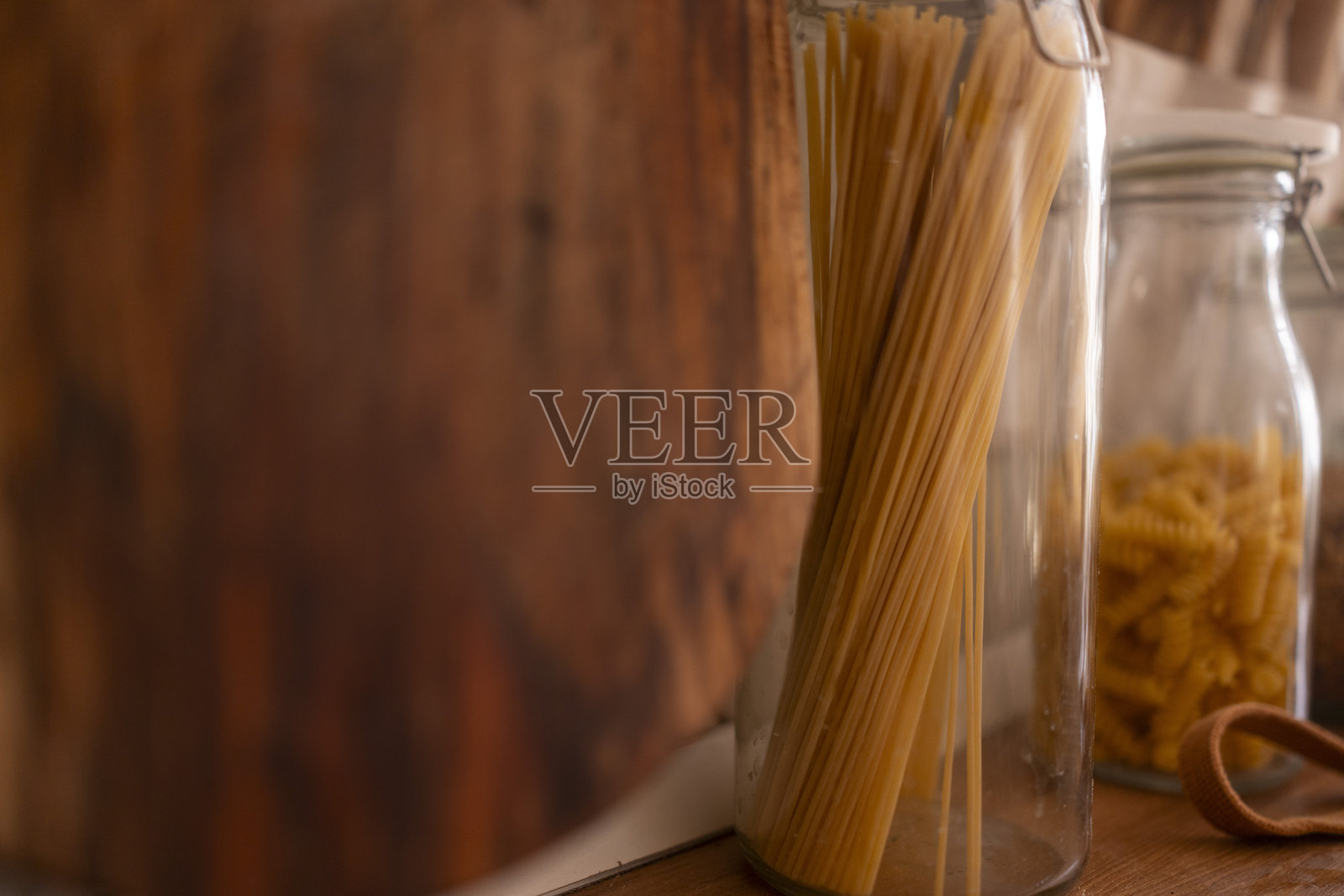 温暖厨房环境中,木质表面上摆放着装有干意面的玻璃罐,特写镜头。照片摄影图片