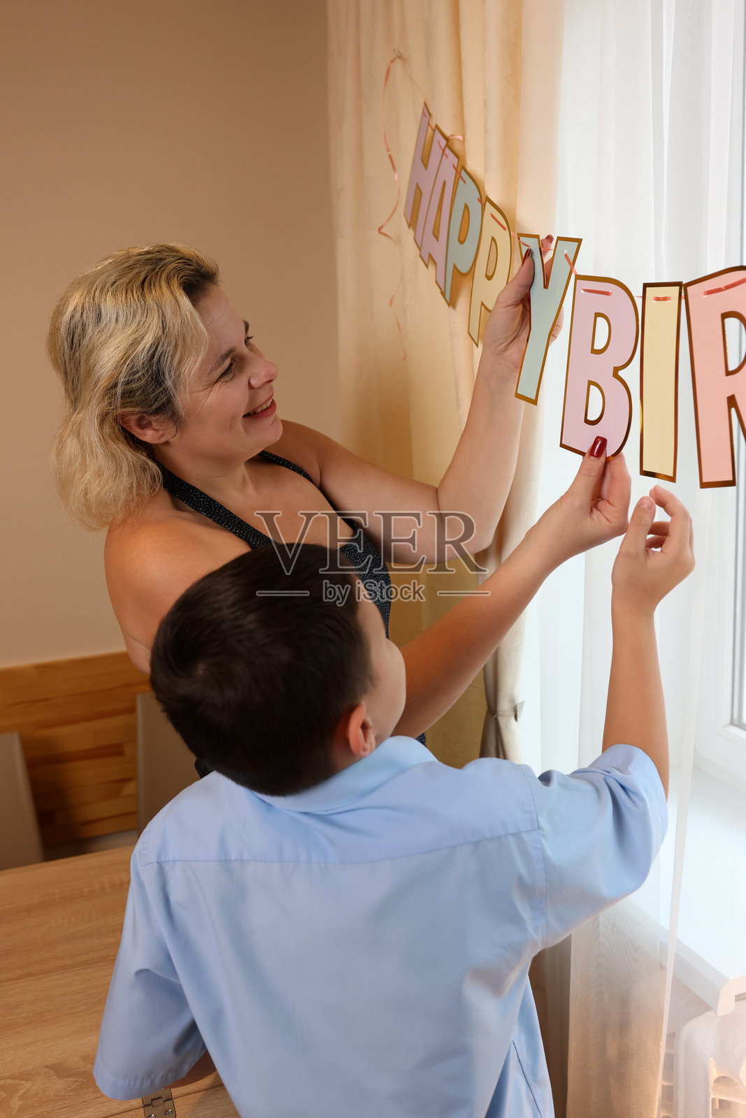 一位女士与她的儿子和侄子一起装饰房间和节日餐桌,为生日庆典做准备。柔和的光线。照片摄影图片