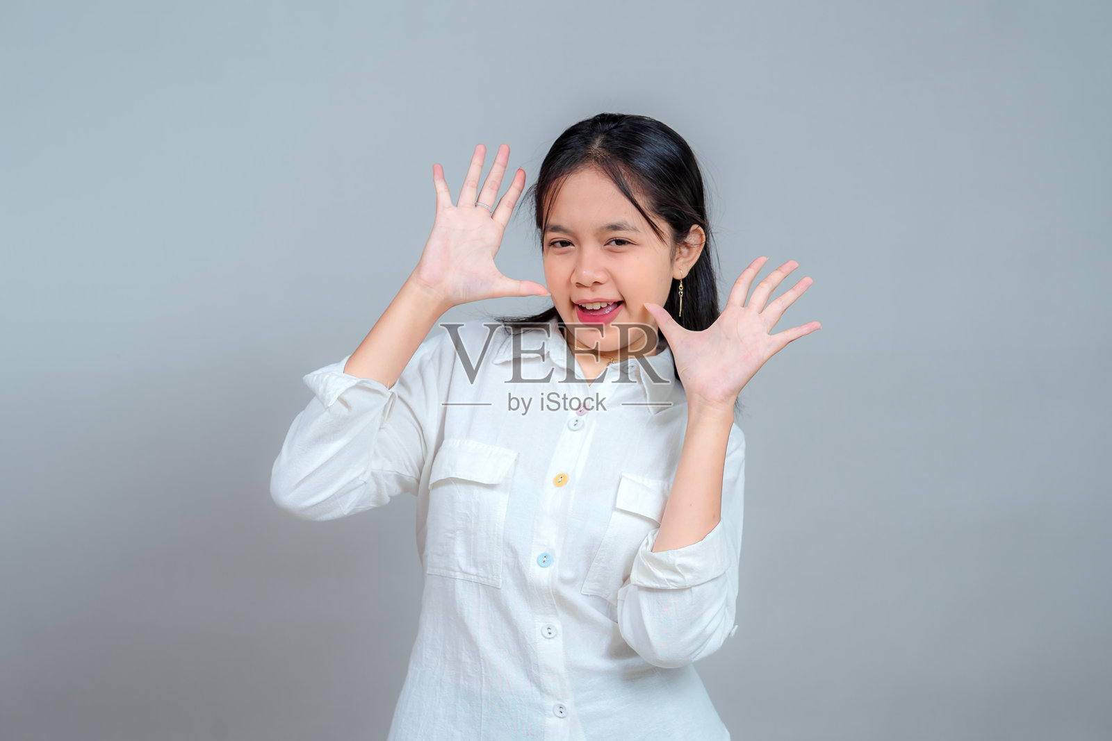 年轻女子在镜头前俏皮地做出双手指势,脸上带着微笑和眨眼,面部表情丰富,姿态充满活力,造型休闲,在影棚内拍摄。照片摄影图片