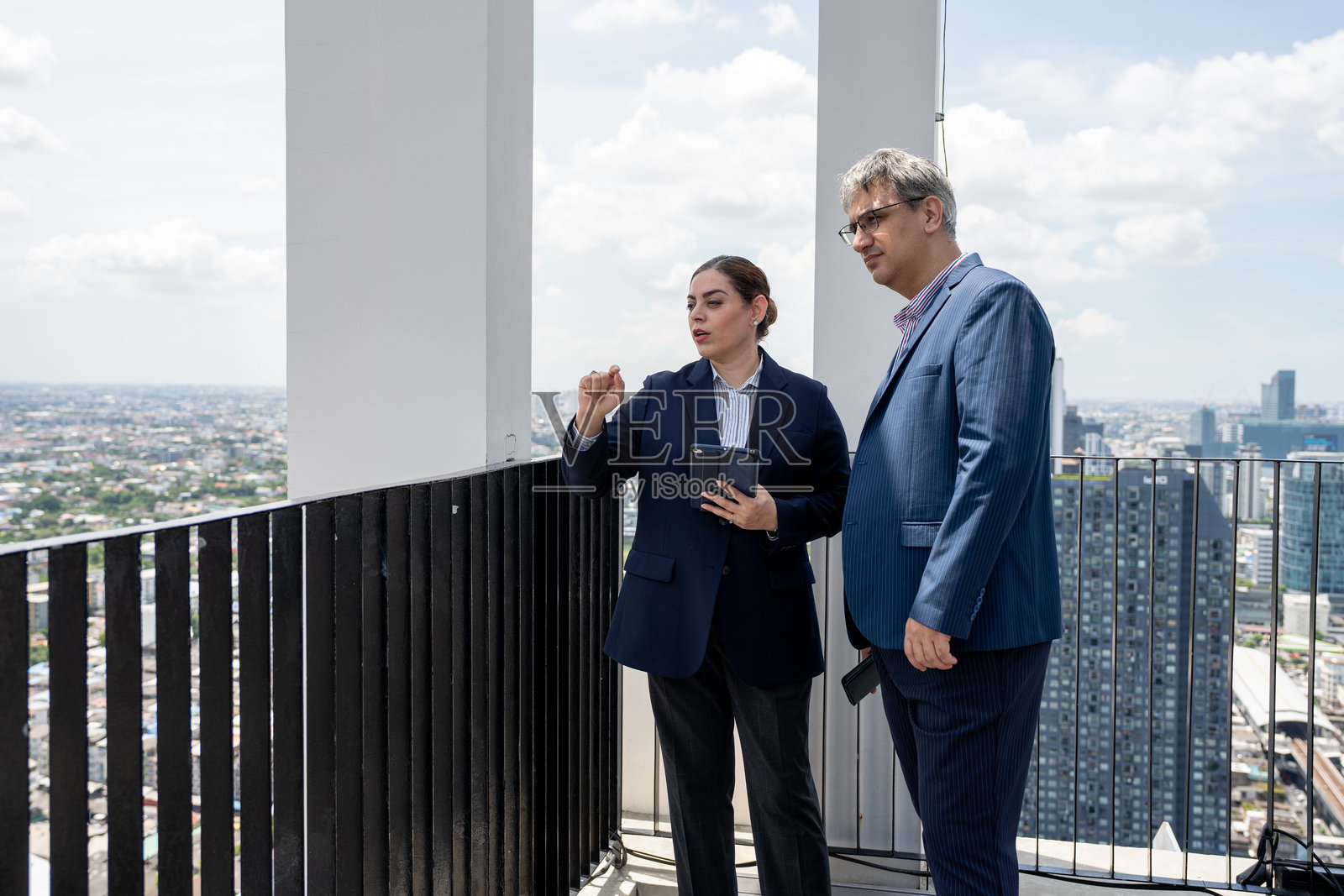 两位商务人士在屋顶办公室使用平板电脑,背景是城市景观。照片摄影图片