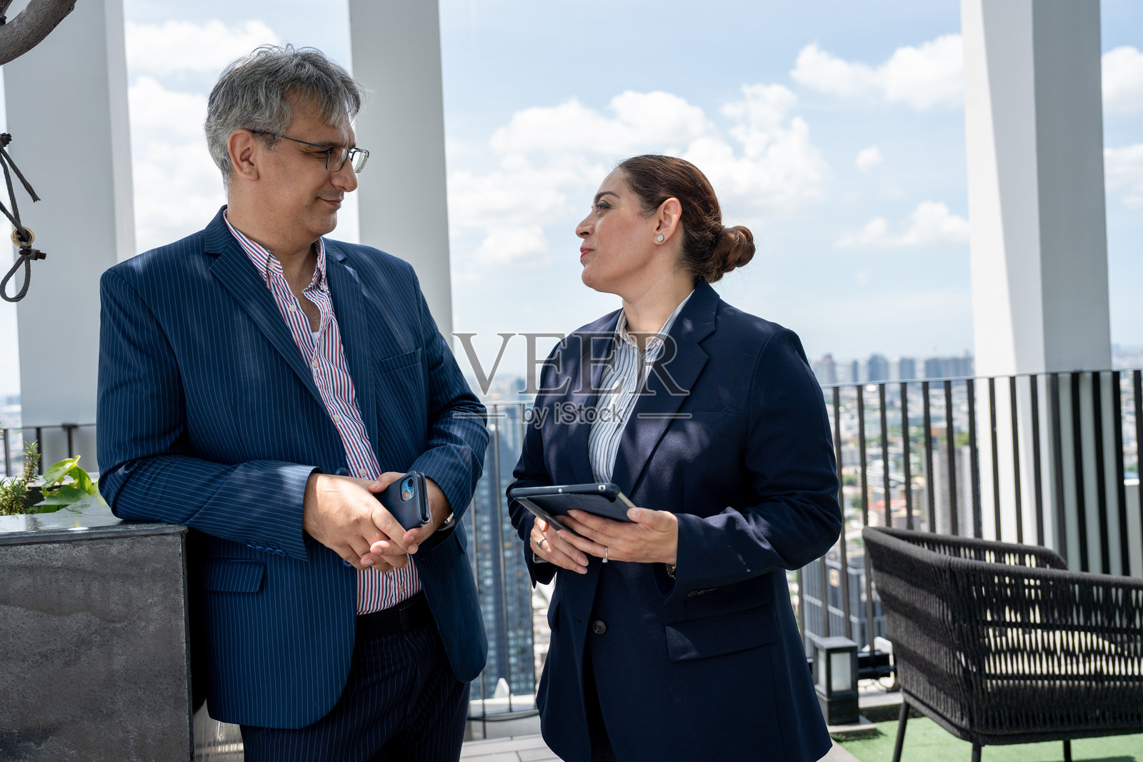 两名商务人士在屋顶办公室使用平板电脑,背景是城市景观。照片摄影图片