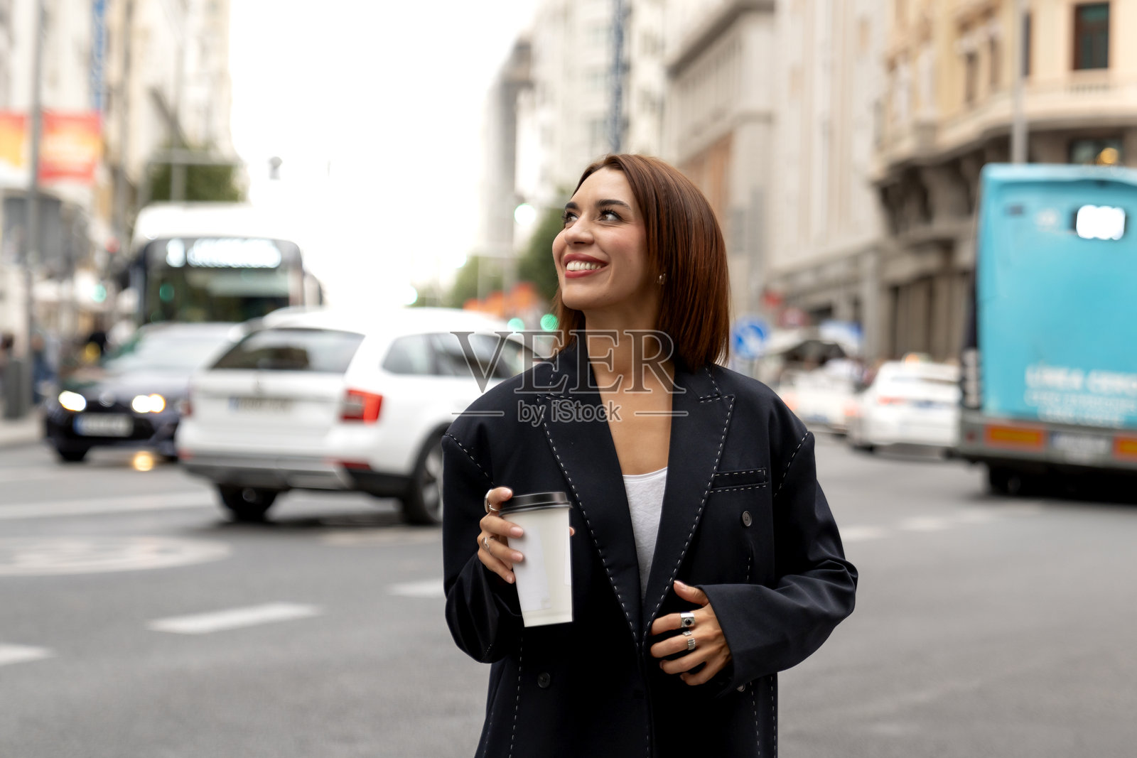 一位自信的女士站在充满活力的城市交通中,手里拿着咖啡杯,脸上带着微笑。照片摄影图片