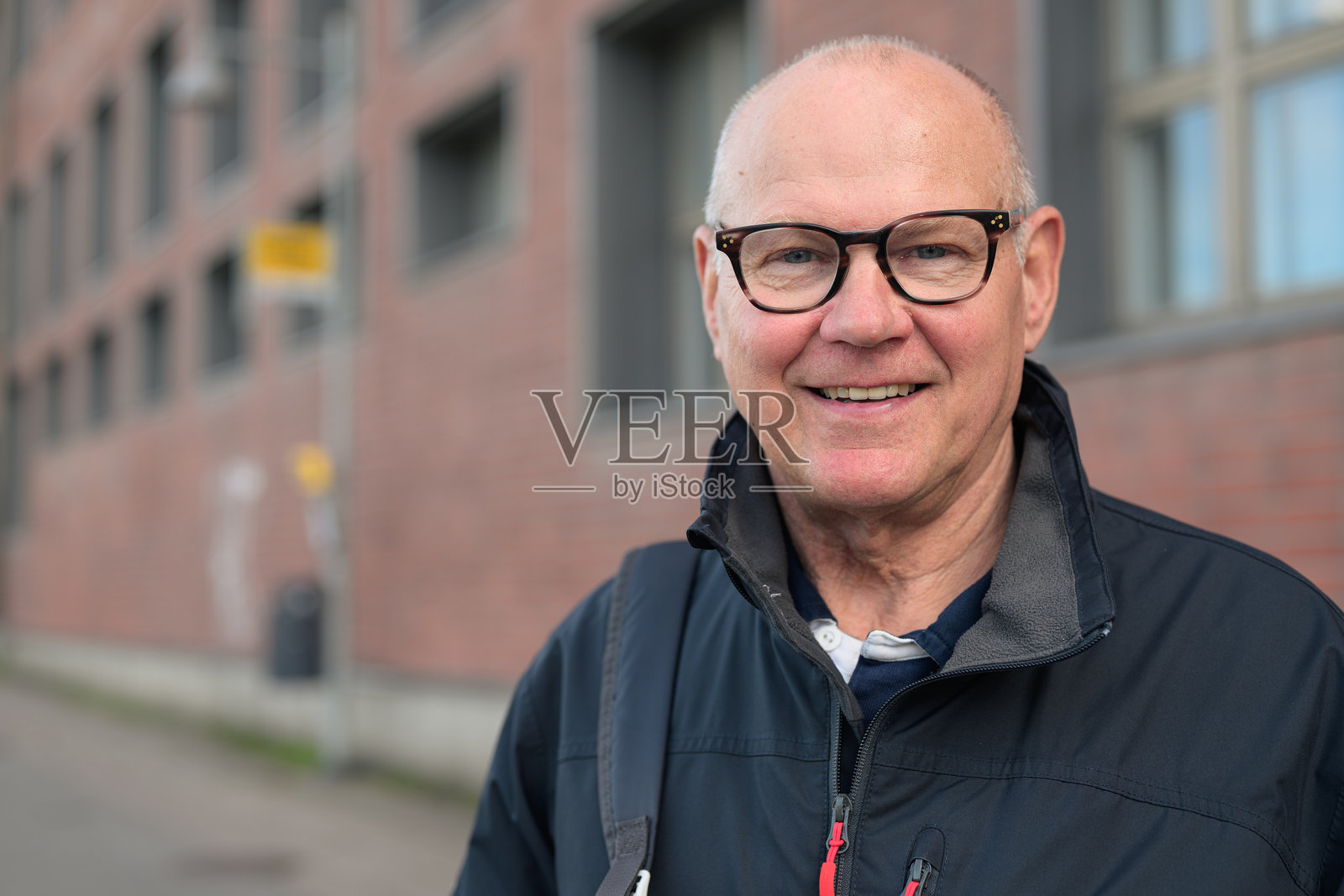 戴眼镜的年长男性在城市公交车站微笑着等待的肖像照片摄影图片