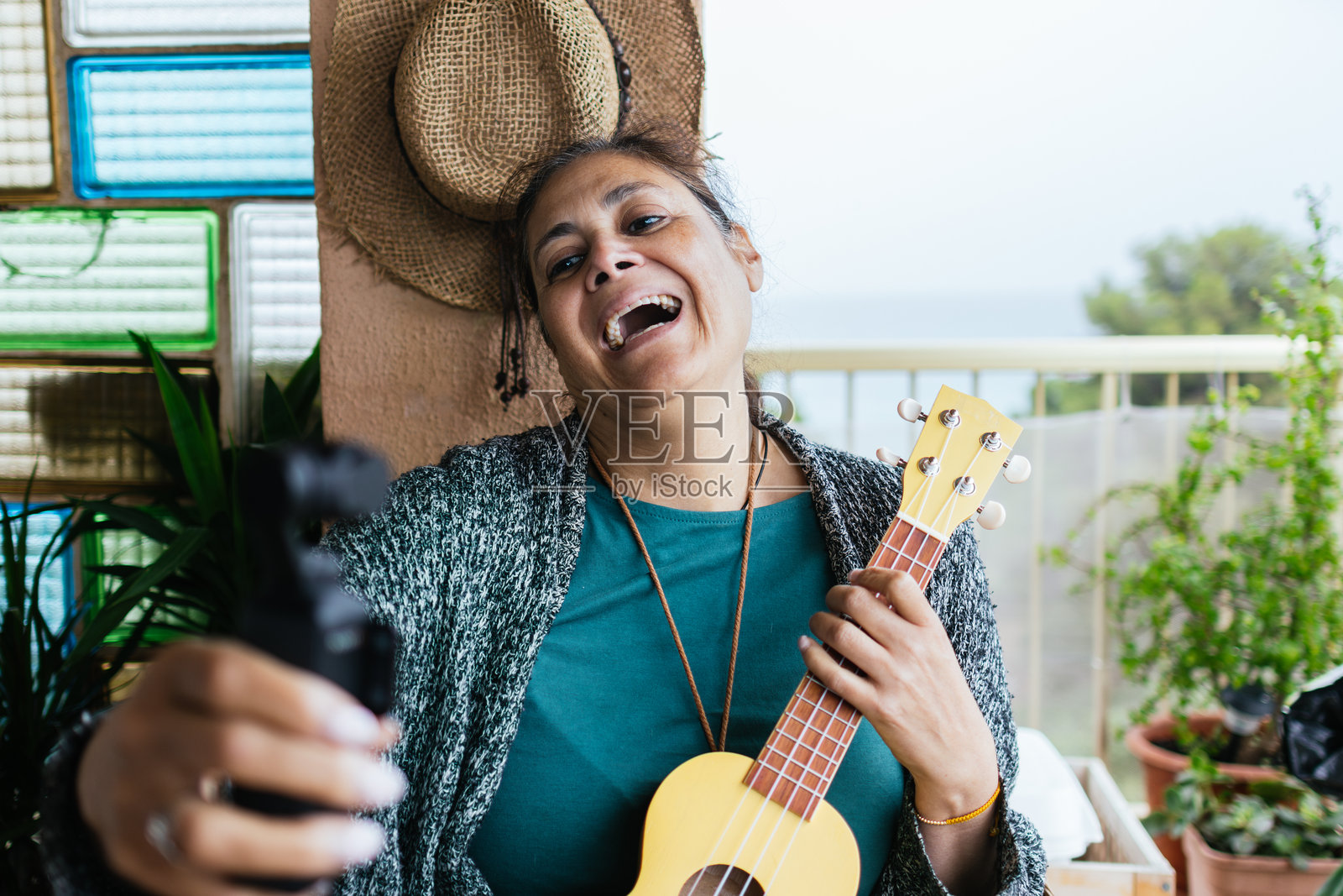 成熟的中东女性网红手持摄像机为社交媒体直播,同时用尤克里里演奏音乐。照片摄影图片