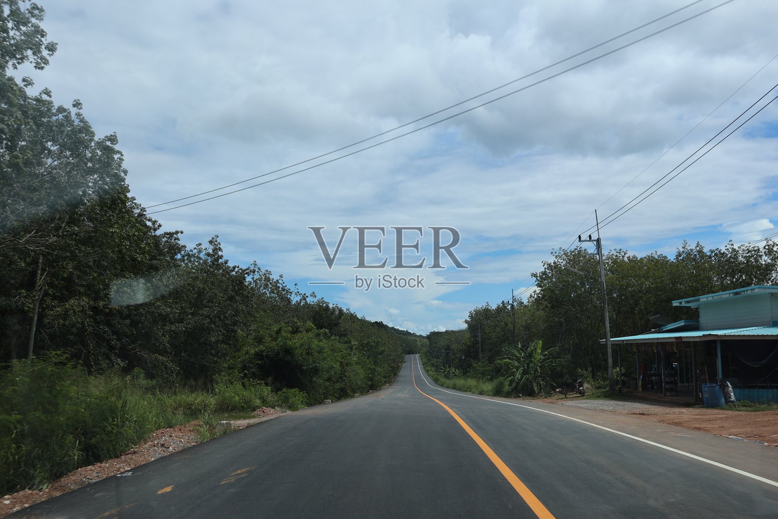 一条荒芜的公路穿过开阔的风景,天空部分多云,远处可见一家商店。照片摄影图片