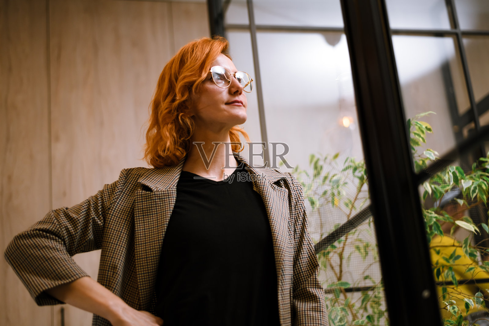 一位自信的橙发女性在白天于城市环境中,在充满绿植的现代建筑内摆姿势照片摄影图片