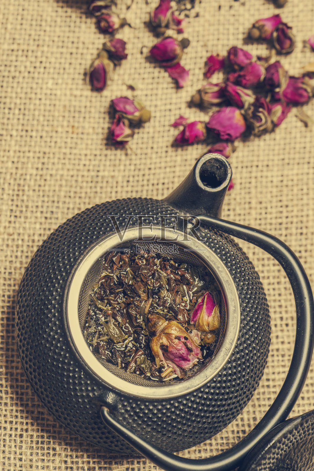 一块粗麻布上放着一个 pretty 亚洲风格的黑色铸铁茶壶和玫瑰花蕾照片摄影图片