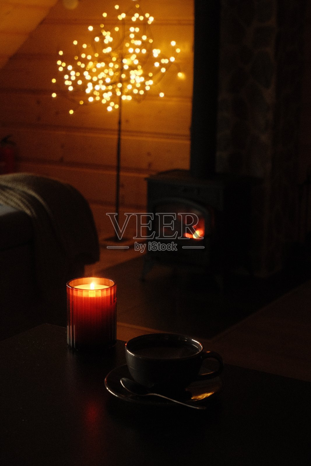 温馨的室内场景,有温暖的烛光、咖啡杯和发光的装饰树灯照片摄影图片